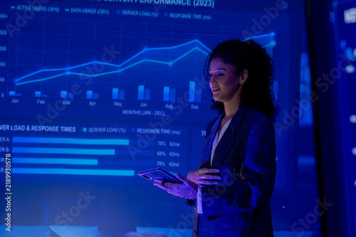 Businesswoman presenting glowing performance dashboard with charts and response metrics during technology meeting, conveying focused confidence in modern office