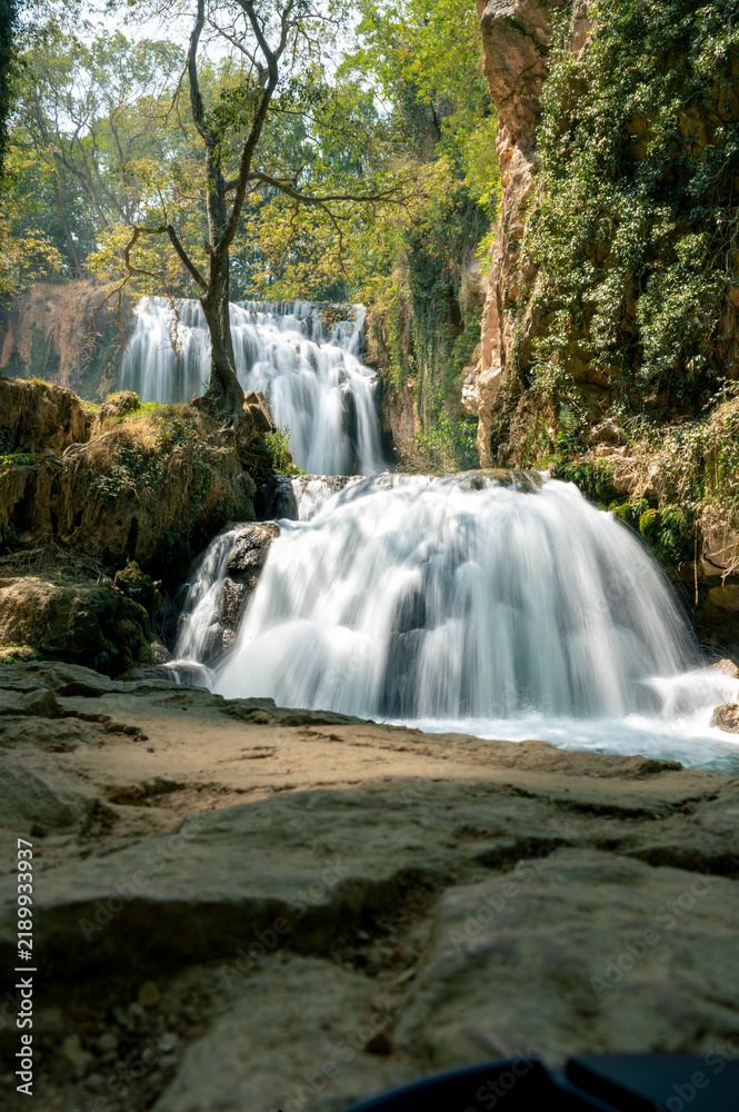 Fototapeta premium A cascade of silky water spreads over travertine steps amid moss and trees in the Monasterio de Piedra natural park in Aragon, Spain, a tranquil long exposure of a flowing waterfall.