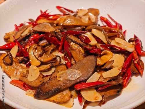 stir-fried porcini mushrooms with dried red chilies and sliced garlic served on a white plate