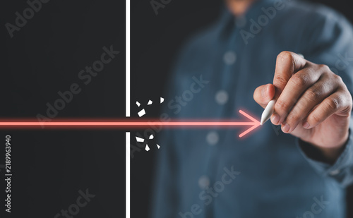 Business breakthrough and overcoming barriers concept with a hand pushing a glowing arrow through an obstacle for innovation, determination, problem solving, progress, success, leadership and growth.