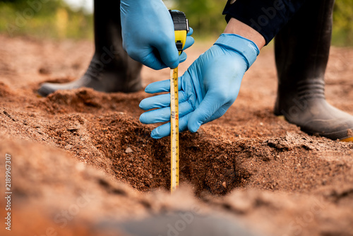 Environmental technician measuring soil pit depth during sample collection for soil quality analysis.
