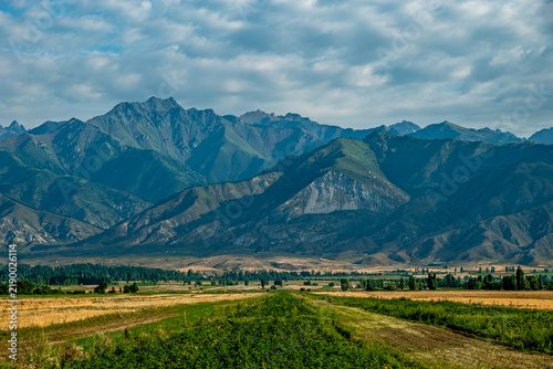 Agricultural fields and rugged mountain range under cloudy sky Kyrgyzstan