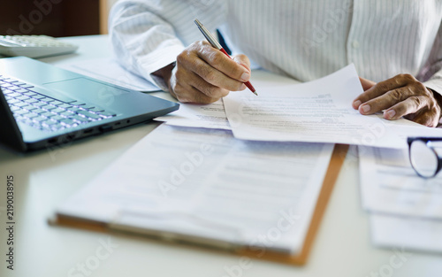 close up shot, asian businessman reviewing document at office working on laptop. professional lawyer reading and checking business documents and contract before giving advice to customers