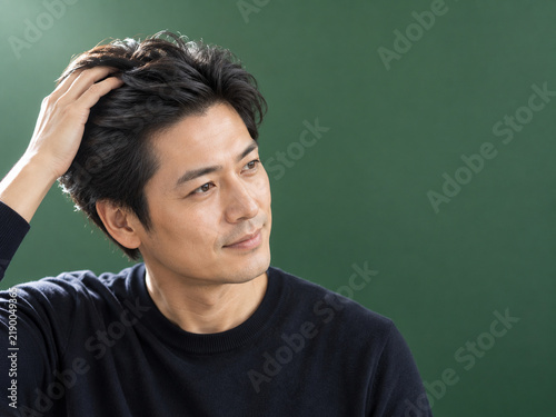濃い緑の背景で指を入れて髪をかき上げる男性