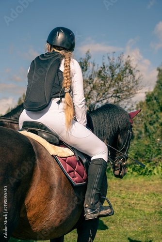 Fotografie Equestrian rider on a dark horse wearing protective riding equipment outdoors