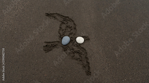Minimalist composition showing two smooth pebbles resting on dark sand with precise gap forming unmistakable shape