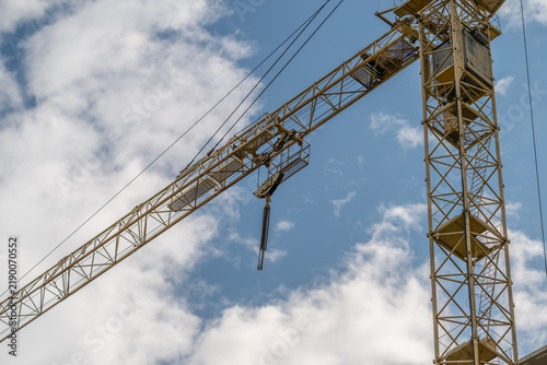 Construction crane towering against a bright blue sky adorned with fluffy clouds during a sunny day