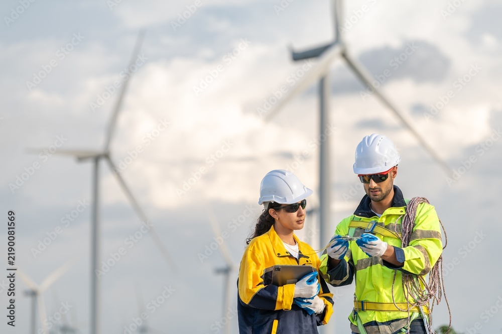 Fototapeta premium Teamwork engineers coaching wind turbine power generator sustainability performance brainstorming together at Renewable Energy Plant Male and female engineers reading compass inspecting windmill