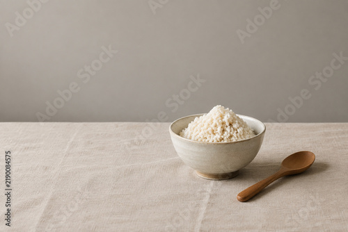 Bowl of koji rice with wooden spoon on linen, minimal food concept