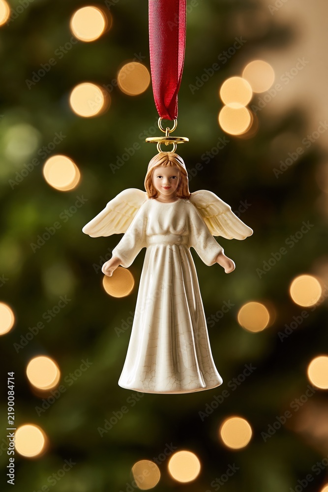 Fototapeta premium Elegant ceramic angel Christmas ornament with halo and wings, hanging against a blurred festive tree background