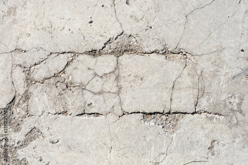 A close up horizontal view shows a rough grey concrete pavement covered with deep cracks and eroded stone sections.