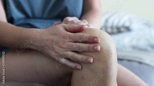 Woman hands gripping painful knee while sitting on bed, closeup of orthopedic joint inflammation