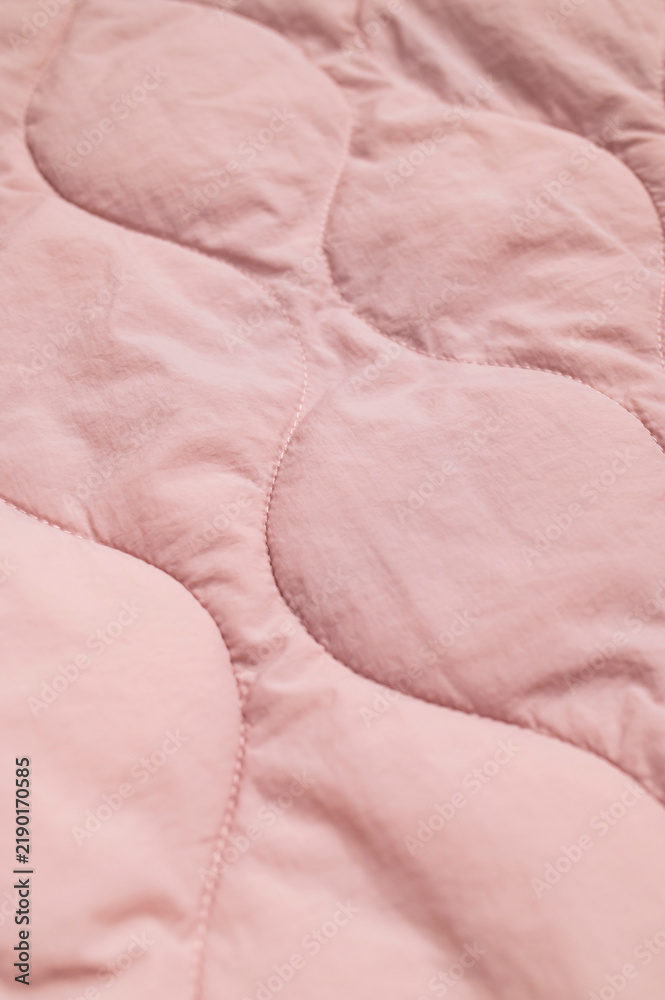 Obraz premium Closeup pink textile shows padded quilting with curved stitched panels and subtle folds. Soft fabric texture suits fashion development, blanket production, interior styling and surface design.