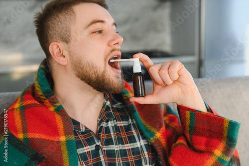 Fotografie Man treating sore throat with oral spray during illness