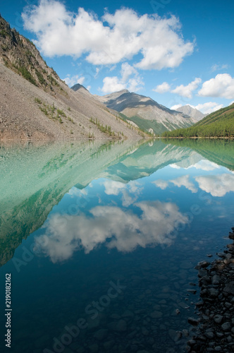 The Lower Shavlinsky lake, glacial lake in the Altai mountains, white clouds mirror themselves in its crystal-clear water in the morning, Russian Federation