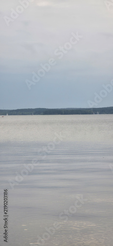 Calm lake water texture with a dark distant shoreline and tiny sails