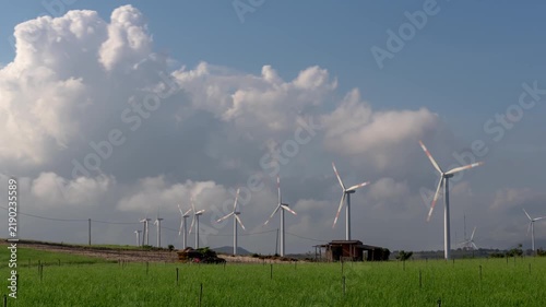 Timelapse of modern wind turbines spinning in a green field under a dynamic blue sky with fluffy white clouds.