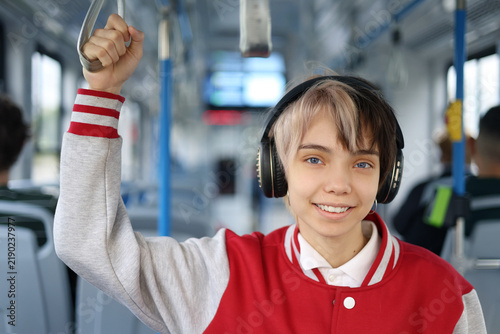 Smiling teenage girl rides a city tram she standing and listening to music through headphones. Urban public transport commute, technology and youth lifestyle concept.