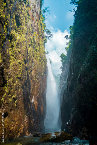 Sunlit slot canyon waterfall framed by rainforest cliffs, Muong Hum, Lao Cai, Vietnam