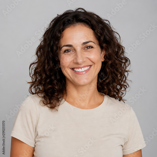 Smiling woman with curly hair poses for a portrait against a gray backdrop