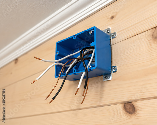 Electrical junction box mounted on wooden wall with exposed wiring and screws