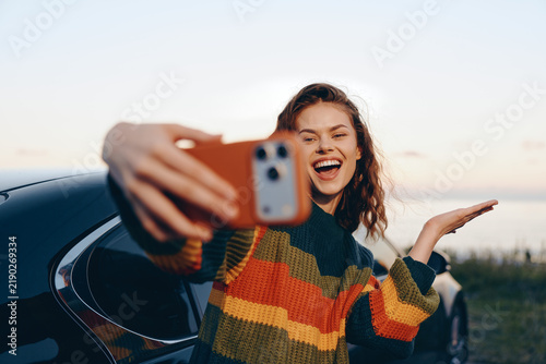 Картината върху платно A cheerful woman takes a selfie beside a car in an open outdoor setting, capturing carefree leisure and spontaneous joy
