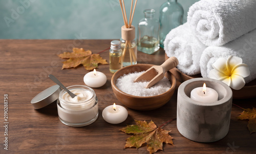 Nourishing cream jar wooden bowl bath salt rolled towels burning candles aromatherapy diffuser bottles autumn foliage floral blossoms serene skin care pampering routine wellness