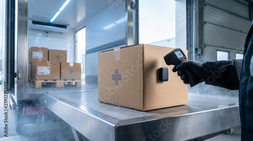 Medical cold chain worker checking the temperature of a pharmaceutical package inside a refrigerated delivery truck at a warehouse, with IoT temperature monitoring technology and cold storage conditio