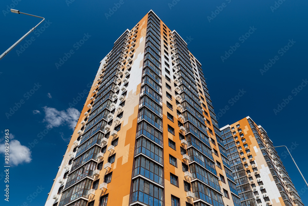Fototapeta premium Modern apartment building reaches into the blue sky on a sunny day with few clouds and street lamps in view