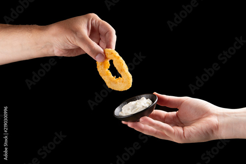 Hand holding fried onion ring over dipping sauce food preparation