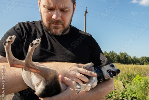 Canvastavla small dog baring its teeth while supported on its back by an owner outdoors, a c