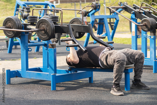 Foto stocky man performs a bench press on public outdoor gym equipment, demonstrating