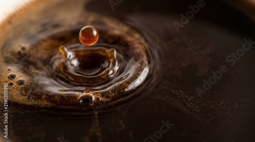 Dark coffee liquid droplet merging into rich pool of beverage creating textured surface