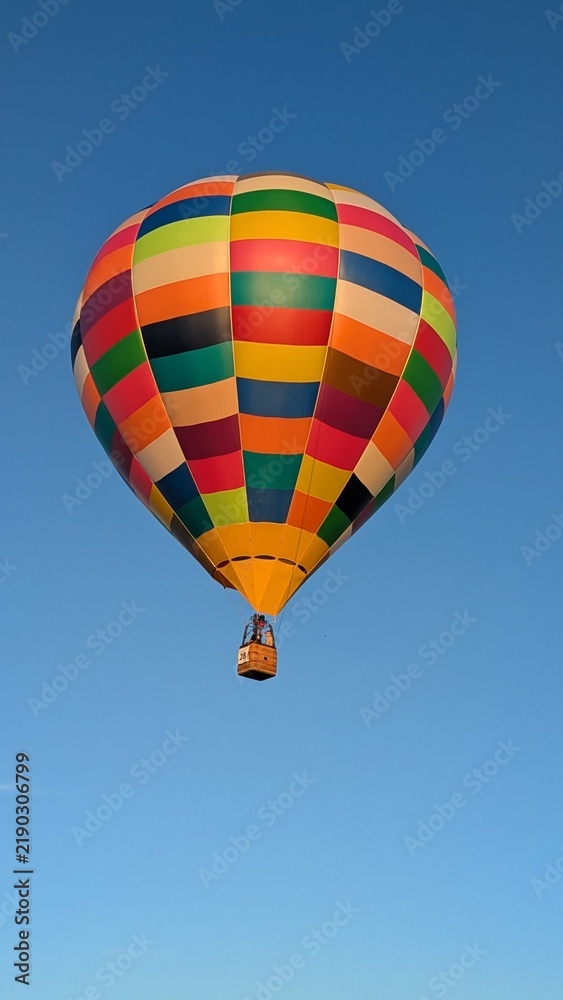 Fototapeta premium Vibrant Colorful Hot Air Balloon Flying High in Clear Blue Sky Skyward View of Patterned Aerostat Envelope and Passenger Wicker Basket for Adventure Travel Aviation and Freedom Concept Background