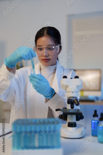 Obraz na płótnie Female scientist in a lab coat and protective eyewear meticulously handling a te