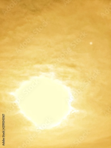 Burning sun radiates a brilliant orange glow, while soft clouds gently drift across the luminous sky. The sunlight creates a dramatic and warm atmosphere, making the scene ideal for themes of energy, 