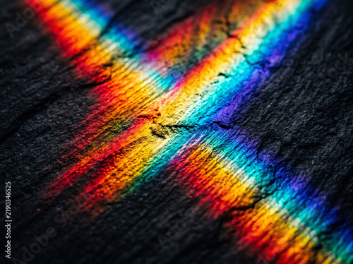 Vibrant rainbow light reflection casting colorful prism rays on dark textured slate background