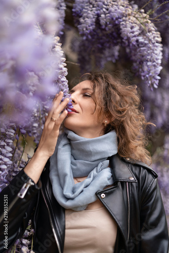 Spring blossoms, beautiful young lady smelling purple wisteria flowers in a blooming garden with a soft romantic mood