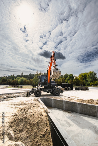 Excavator operates at a rental site, moving dirt for landscaping project. The machine digs and shapes the ground in preparation for further work