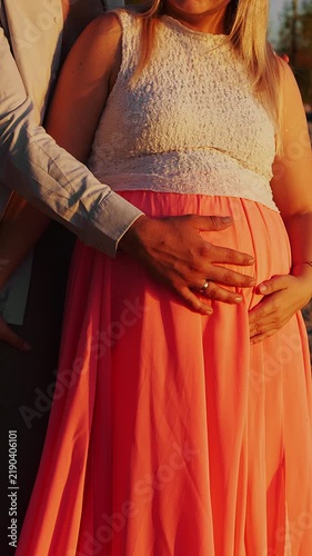 Close-up of expecting parents gently holding pregnant belly together in warm sunset light. Tender family moment representing pregnancy, parenthood and anticipation.