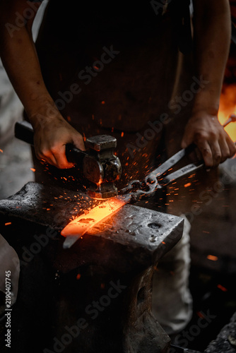 Fotografía Blacksmith hammering glowing red-hot steel on anvil with tongs and flying sparks