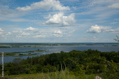 Peaceful summer landscape of the Dnipro River with islands, green forest and grass, distant wooded shore, blue sky and white clouds