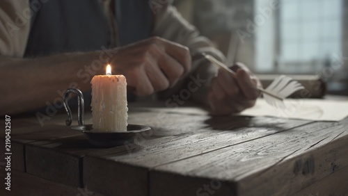 Foto Burning candle in a metal holder on a rustic wooden table with hands of a mediev
