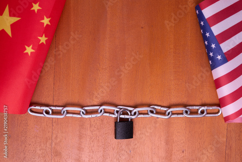 US and China flags with locked chain on wooden table for trade war economic sanction and tariff policy concept