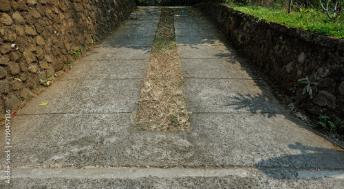 Foto Parallel concrete vehicle tracks leading up an inclined path bordered by natural stone retaining walls in daylight