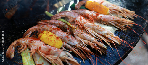 Prawns grilling on round cast iron barbecue with open fire flame. Fresh shrimp with lemon on charcoal grill. Outdoor cooking seafood on fire concept.