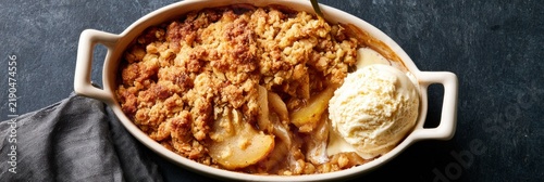 Pear crumble served in an oval dish with crumbly topping and vanilla ice cream on the side in a warm kitchen atmosphere.