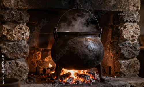Smoking black witch cauldron hanging over fireplace for dark Halloween scene