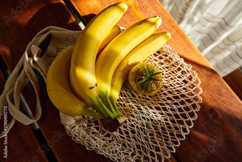 Bananas and a round fruit in a net bag on a wooden table in sunlight