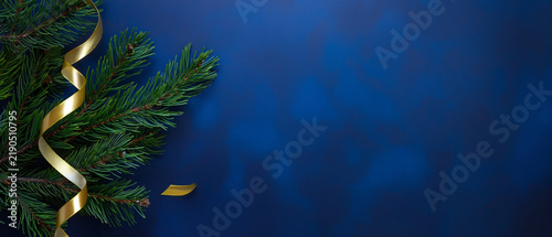 Christmas background with fir branches and golden ribbon on dark blue surface with copy space